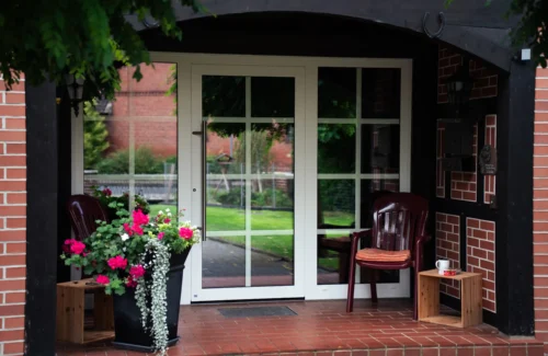 Dreiteilige Haustür aus Glas mit weißem Rahmen in roter Steinmauer.