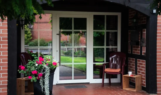 Dreiteilige Haustür aus Glas mit weißem Rahmen in roter Steinmauer.