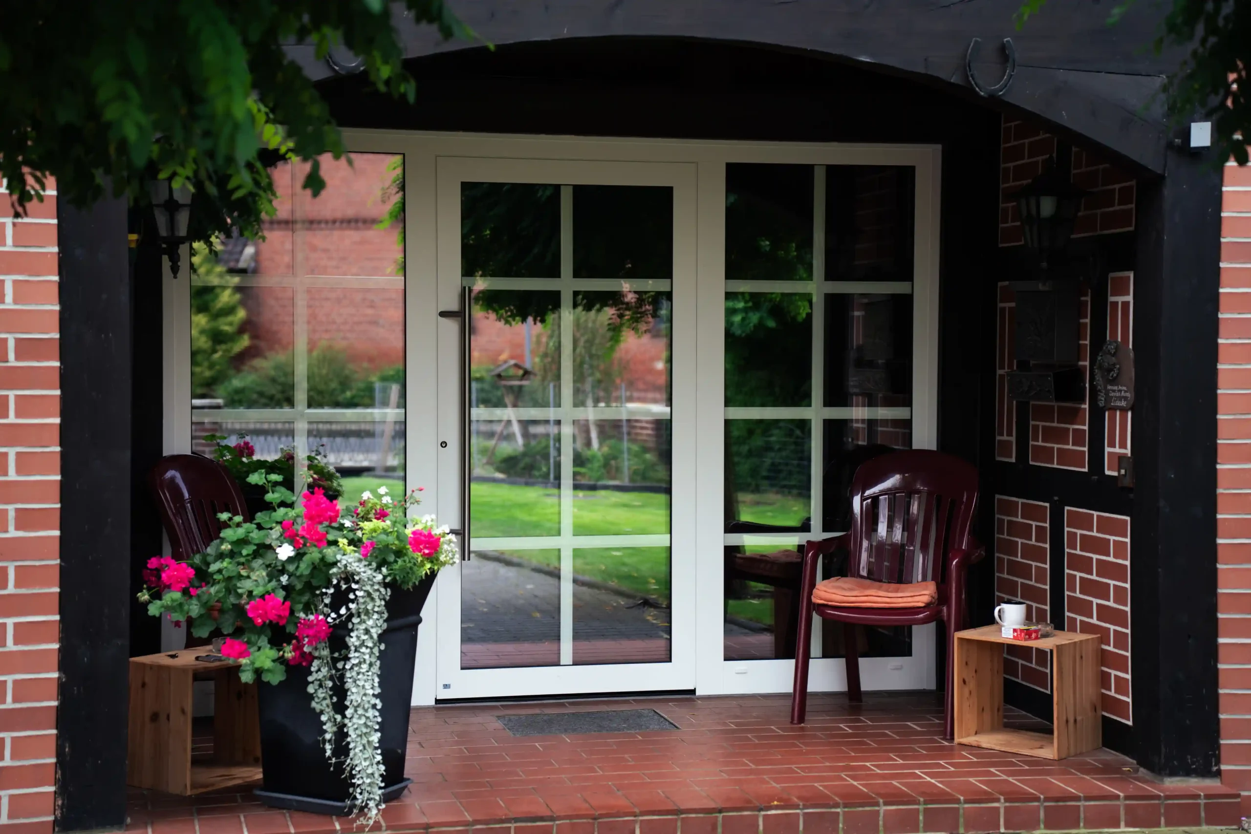 Dreiteilige Haustür aus Glas mit weißem Rahmen in roter Steinmauer.